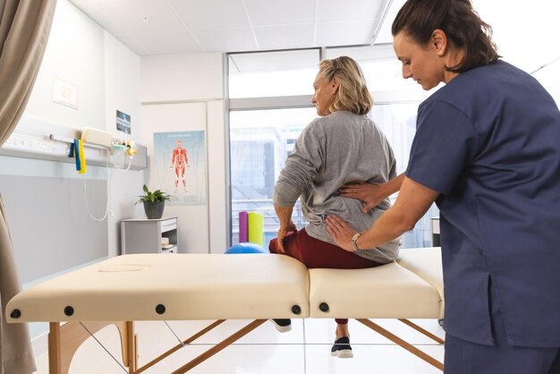 Foto fisioterapeuta caucásica y mujer mayor masajeando la espalda en el hospital