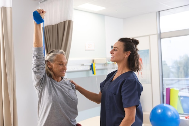 Foto fisioterapeuta caucásica y mujer mayor que usa banda de ejercicio estirando los brazos