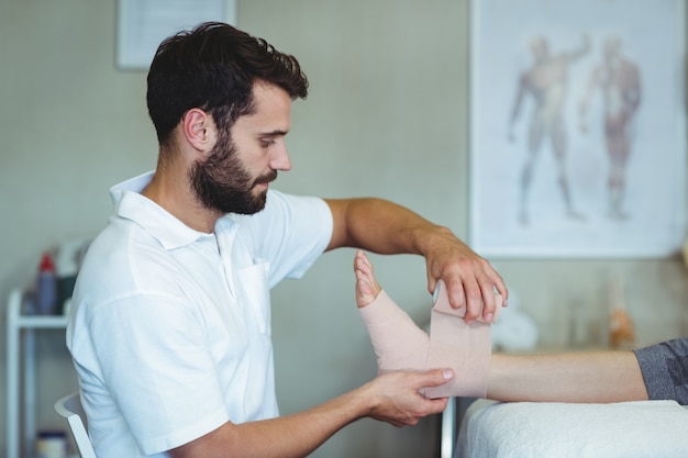 Foto fisioterapeuta colocando una venda en los pies lesionados del paciente