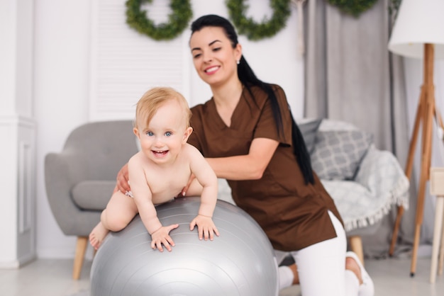 Fisioterapeuta com bebê feliz fazendo exercícios com bola de ginástica na sala médica. Conceito de saúde e médico.