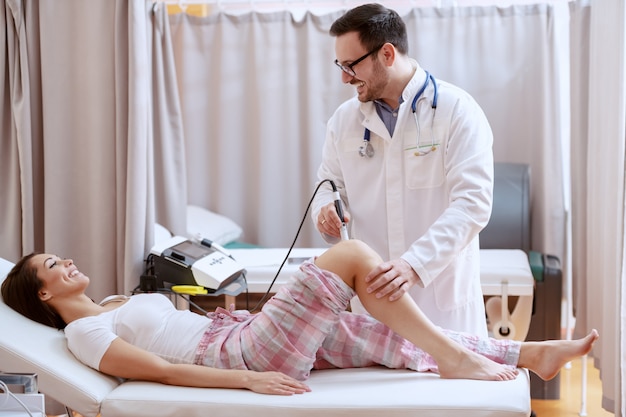 Fisioterapeuta dando tratamento médico à sua paciente do sexo feminino com dispositivo de eletrólise. Interior do hospital.