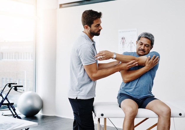 Fisioterapeuta de estiramiento y hombre maduro en la clínica ayudando y cuidado de la salud con ejercicio y fitness Hospital entrenamiento y fisioterapia de rehabilitación del paciente y concentración de la persona