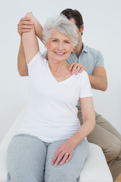 Fisioterapeuta estirando el brazo de una mujer senior sonriente