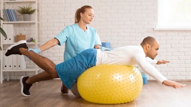 Foto fisioterapeuta femenino ayudando a paciente masculino en bola