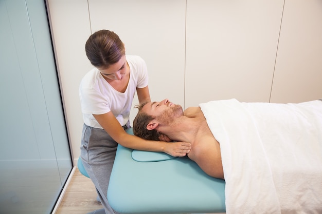 Fisioterapeuta femenino dando masaje de cabeza al paciente masculino