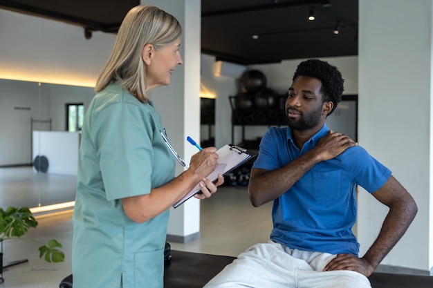 Fisioterapeuta feminina a falar com um paciente masculino e a fazer anotações