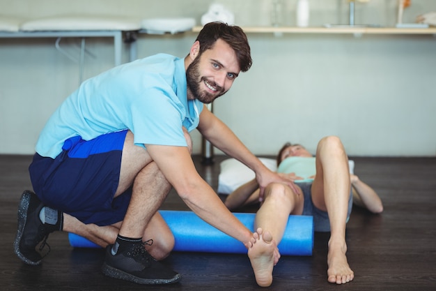 Fisioterapeuta haciendo terapia de piernas a una mujer usando un rollo de espuma