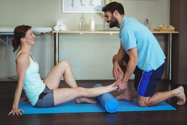 Fisioterapeuta haciendo terapia de piernas a una mujer usando un rollo de espuma