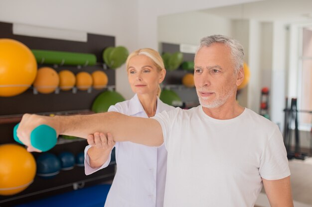 Fisioterapeuta loira auxiliando um paciente do sexo masculino durante o treino