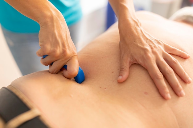 Una fisioterapeuta masajea la espalda de un hombre mayor con una herramienta de masaje