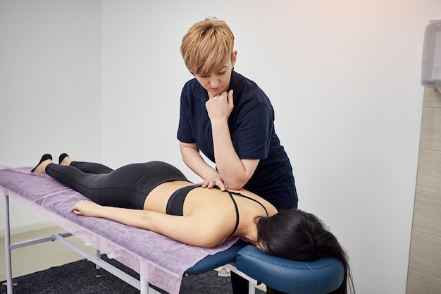 Fisioterapeuta masajeando a una paciente deportista con músculos dañados en la clínica de kinesio Tratamiento de lesiones deportivas