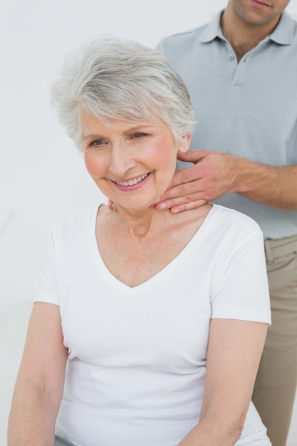 Fisioterapeuta masculina massageando o pescoço de uma mulher sênior