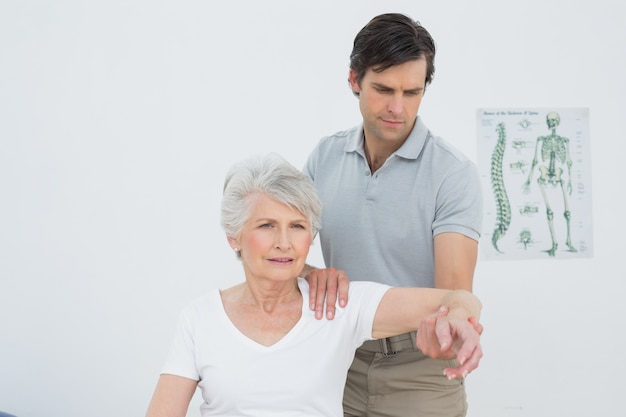 Fisioterapeuta masculino estirando un brazo de mujer senior