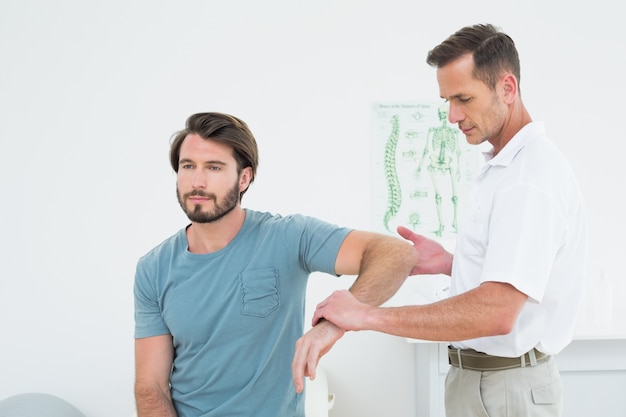 Fisioterapeuta masculino examinando un brazo de hombre joven