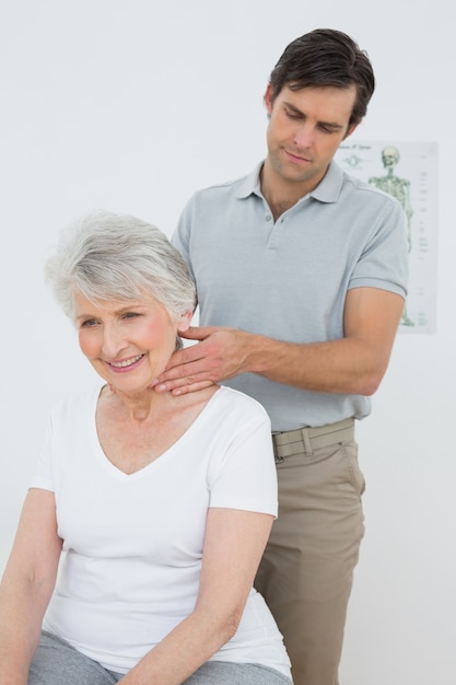 Fisioterapeuta masculino masajeando el cuello de una mujer mayor