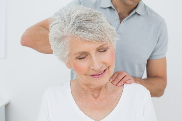 Fisioterapeuta masculino masajeando el cuello de una mujer mayor