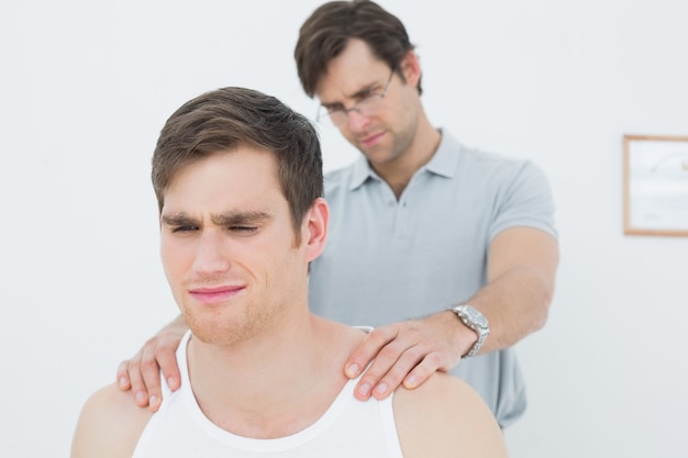 Fisioterapeuta masculino masajeando un hombro joven hombre