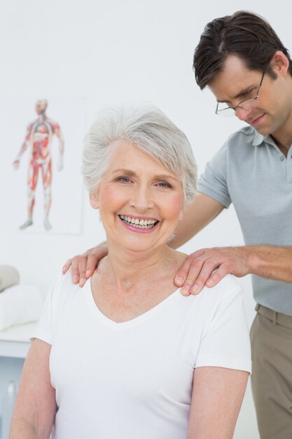 Fisioterapeuta masculino masajeando los hombros de una mujer senior