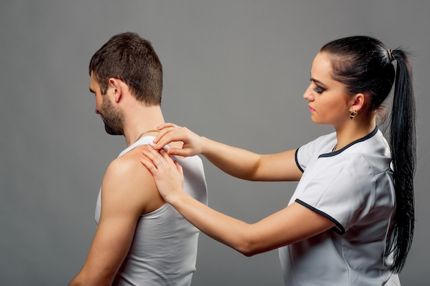 Fisioterapeuta mujer en bata blanca examinando mans atrás aislado en gris