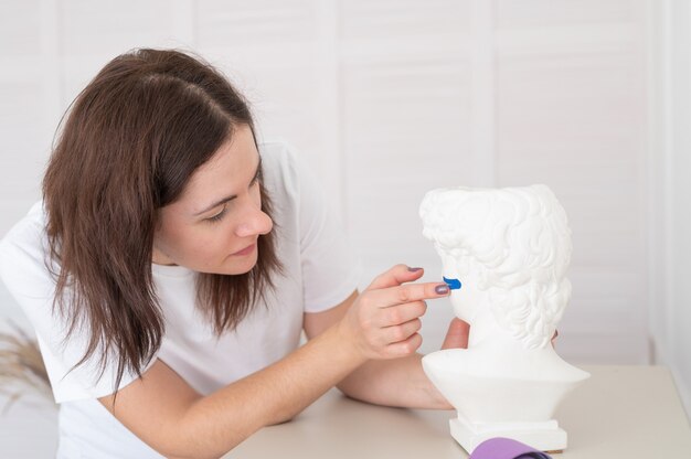 Fisioterapeuta o cosmetólogo colocando cinta de kinesio en la estatua de yeso de la cabeza. Procedimiento anti-envejecimiento. Cinta estética.