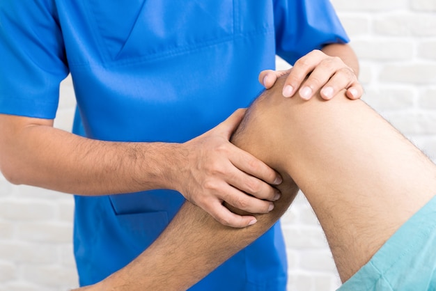 Foto fisioterapeuta que trata la rodilla lesionada de un paciente masculino en el hospital