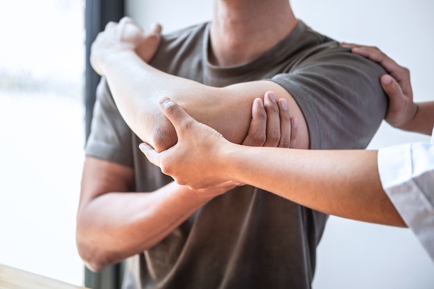 Fisioterapeuta trabajando examinando el tratamiento del brazo lesionado del paciente masculino atleta