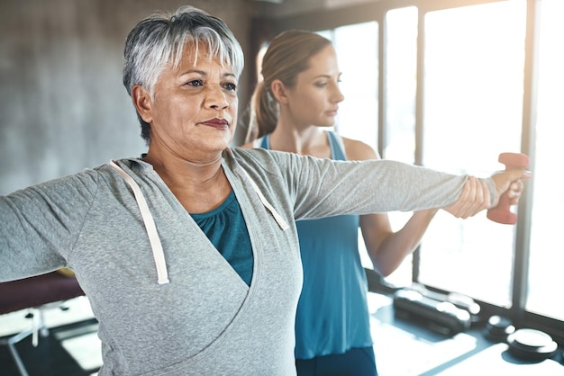 Fisioterapia com halteres e idosa com personal trainer para fitness, bem-estar ou reabilitação Exercício de saúde ou aposentadoria com paciente sênior e fisioterapeuta na academia para treinamento de suporte