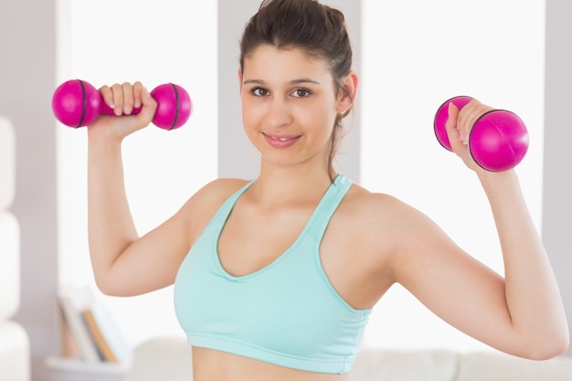 Fit brunette segurando dumbbells sorrindo na câmera