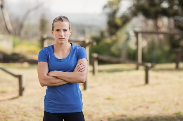 Fit Frau, die mit verschränkten Armen im Bootcamp an einem sonnigen Tag steht