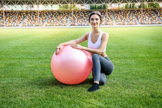 Fit frau mit ball draußen. junge brünette frau posiert mit fitball im freien