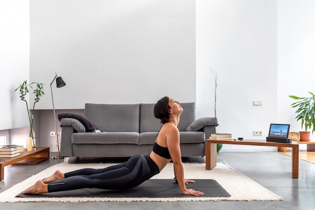 Fit Frau üben Cobra Pose mit Online-Yoga-Trainingsprogramm in der Tablette zu Hause