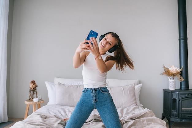 Fit gesunde kaukasische junge Frau in weißem T-Shirt und Blue Jeans verwendet Kopfhörer macht selfie nach Hause Hübsches hispanisches Mädchen macht Videoanruf vom Hotelzimmer genießt Urlaub Jugend- und Reiseurlaub