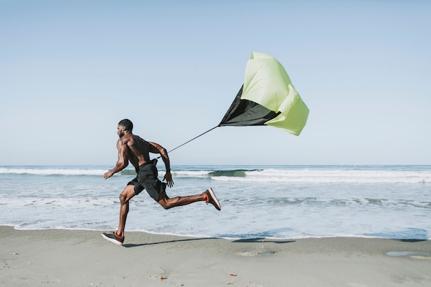 Fit homem com um pára-quedas correndo na praia