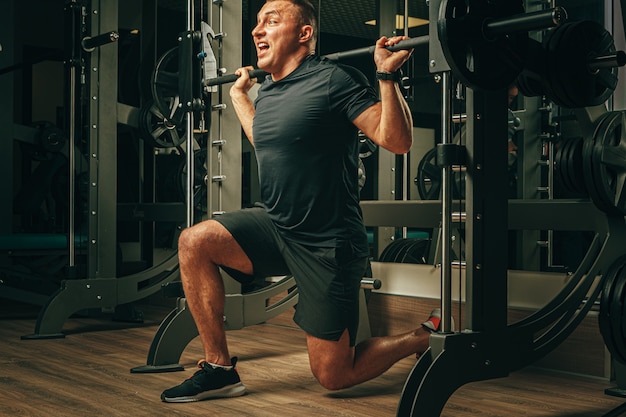 Fit homem fazendo agachamentos em uma máquina de treino