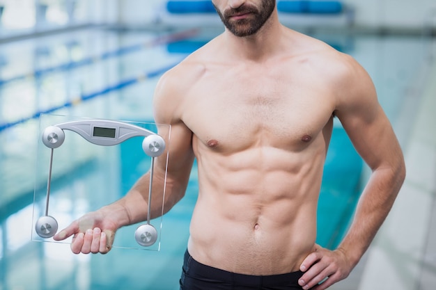 Fit homem segurando uma balança de pesagem na piscina