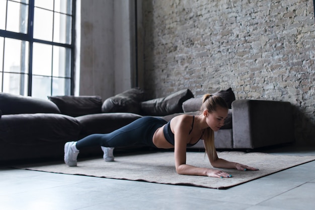 Fit junge frau, die sportbekleidung trägt, die zu hause trainiert, plankingübung auf teppich machend