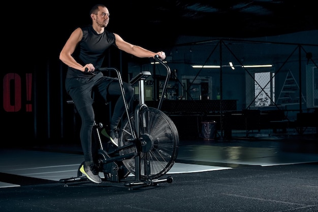 Fit junger Mann mit Heimtrainer im Fitnessstudio. Fitness-Mann mit Air-Bike für Cardio-Training im Cross-Training-Fitnessstudio.