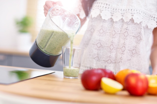 Fit lächelnde junge Frau, die einen gesunden Smoothie in der modernen Küche zubereitet