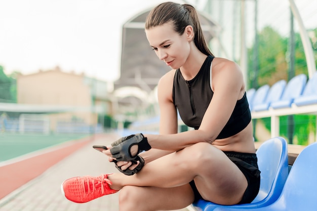 Fit mujer deportiva utiliza el teléfono en el estadio en la mañana durante el entrenamiento físico