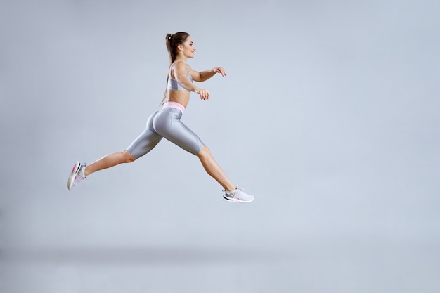 Fit mujer haciendo entrenamiento cardiovascular en el gimnasio. Mujer en ropa deportiva está saltando. Concepto de gimnasio. Aislado en gris