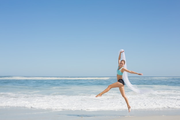 Fit mujer saltando con gracia en la playa con bufanda