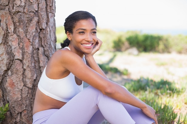 Fit mujer sentada contra árbol sonriendo