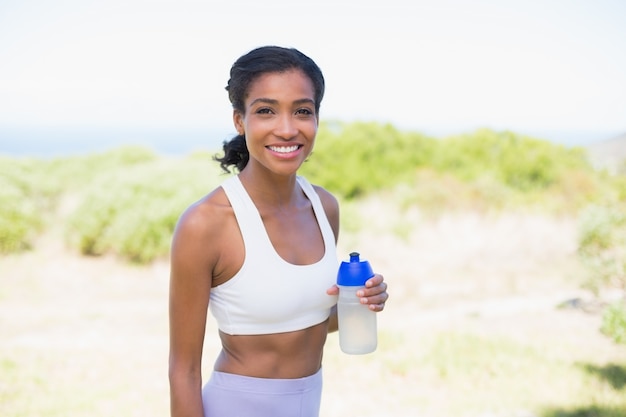 Fit mujer sosteniendo la botella de los deportes sonriendo a la cámara