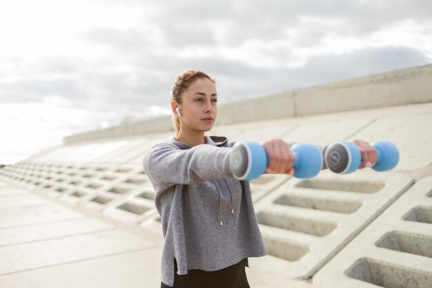 Fit schlanke Sportlerin trainiert Armmuskulatur mit Hanteln im Freien Gesunder Lebensstil Fitness Bodybuilding