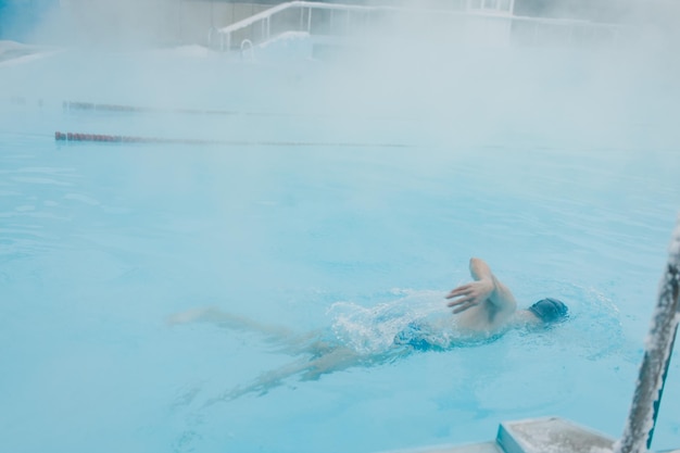 Fit Schwimmer männlich Training Schwimmen im offenen Winterschwimmbad mit Nebel Geothermisches Spa-Konzept im Freien