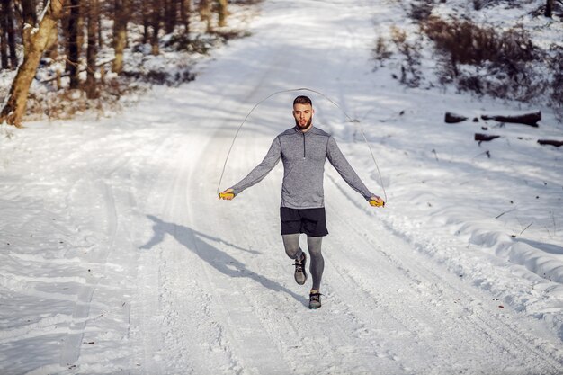 Fit Sportler, der das Seil auf Spur in der Natur am verschneiten Wintertag springt.