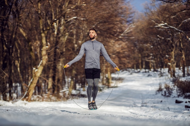 Fit Sportler, der das Seil im Wald am verschneiten Wintertag springt. Gesundes Leben, Winterfitness, Sportbekleidung