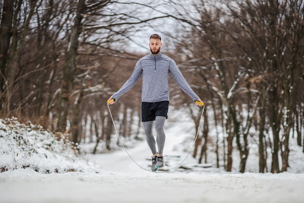 Fit sportler, die am verschneiten wintertag das seil in der natur springen. winterfitness, cardio-übungen