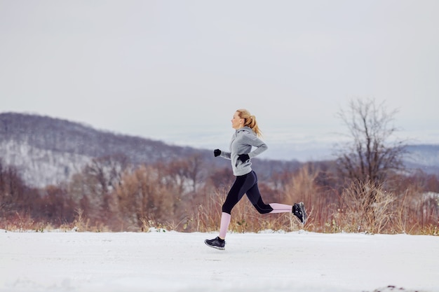 Fit Sportlerin, die am verschneiten Wintertag schnell in der Natur läuft. Gesundes Leben, Naturfitness, Wintersport