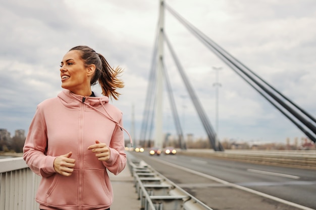 Fit Sportlerin im Trainingsanzug beim Joggen auf der Brücke bei bewölktem Wetter.